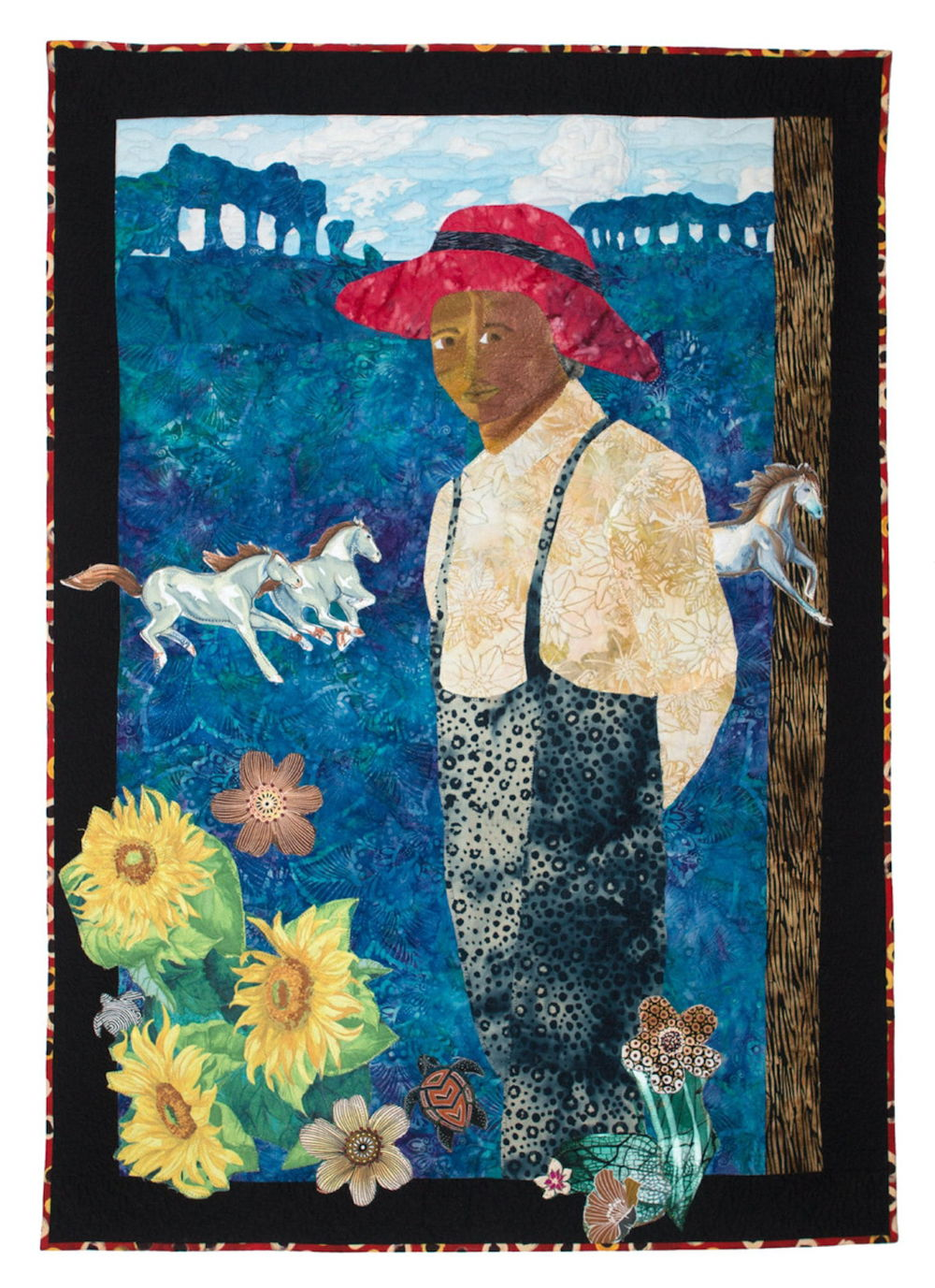 A colorful quilt depicting a Black figure wearing overalls and a red hat looking out at the viewer. Behind the figure, three white horses run across the vast blue landscape. There are flowers at the person's feet.