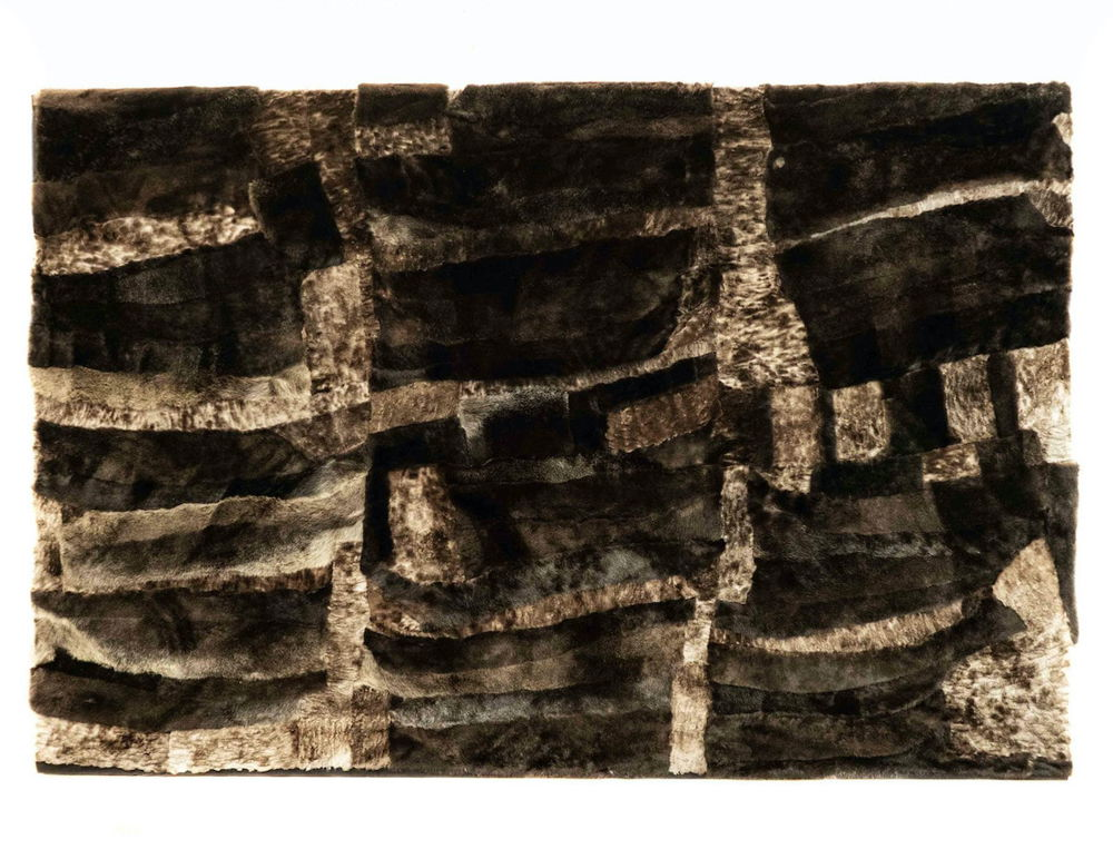 A wall hanging made of brown and gray furs layered on top of one another to form an abstract pattern.