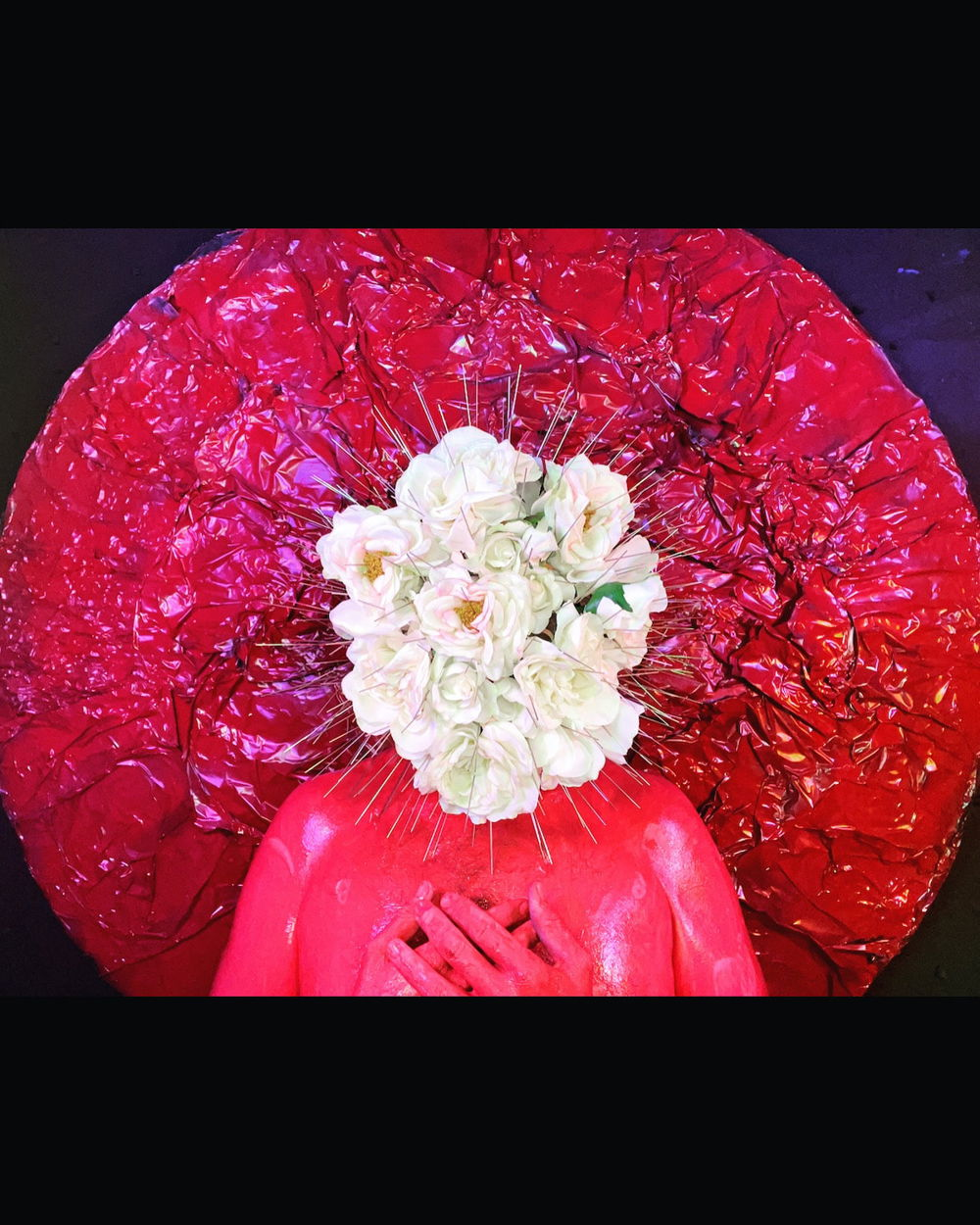 A portrait of a person, painted bubblegum pink, their face obscured by a burst of white flowers. The figure is placed in front of a magenta circle, creating the illusion of a halo and clasps their hands gently at their chest.