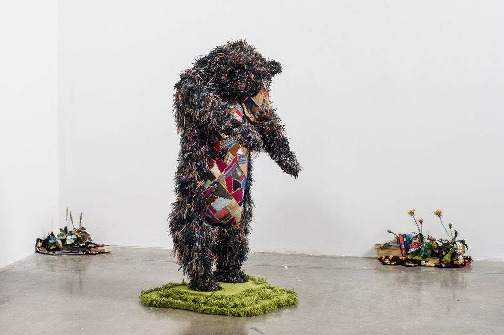 <em>The Bear with Weeds</em>, 2013. Pelt of shredded gay pornography, vintage crazy quilt, thread, plaster, wire armature, dyed chenille blanket; romance novels, gay erotica, afghan blankets, digital textile prints of 'gay encounter' stories on silk, dimensions 59 × 32 × 27 inches.