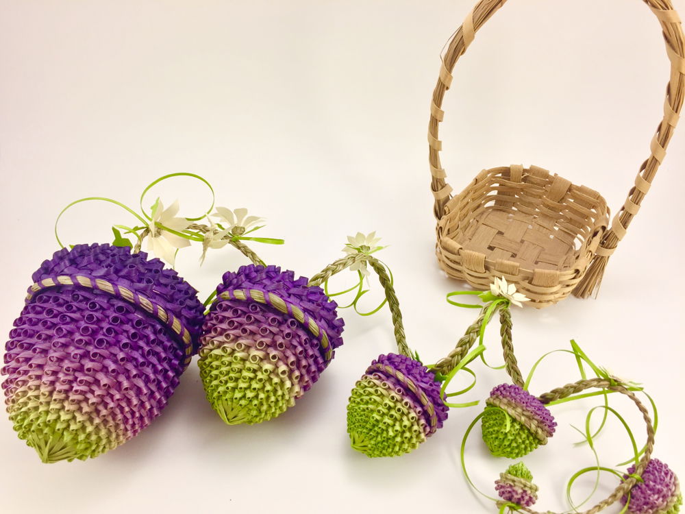 Photo of a group of miniature lidded baskets woven to resemble strawberries and blackberries. The baskets are dyed bright purples and reds with hints of green, with tiny woven flowers and braided grass vines bouncing from the lids of each basket