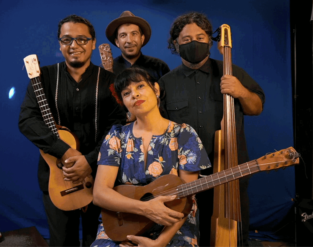 A group of four musicians poses with jaranas and other stringed instruments.