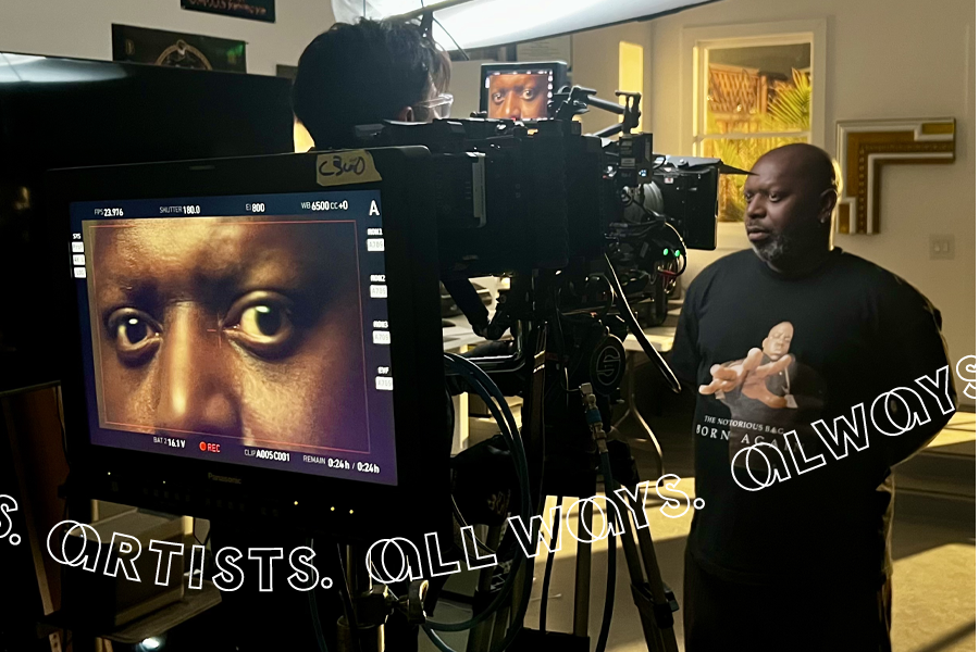 A bald Black man with a beard stands in front of a camera set up. The screen reveals a close up of his eyes.