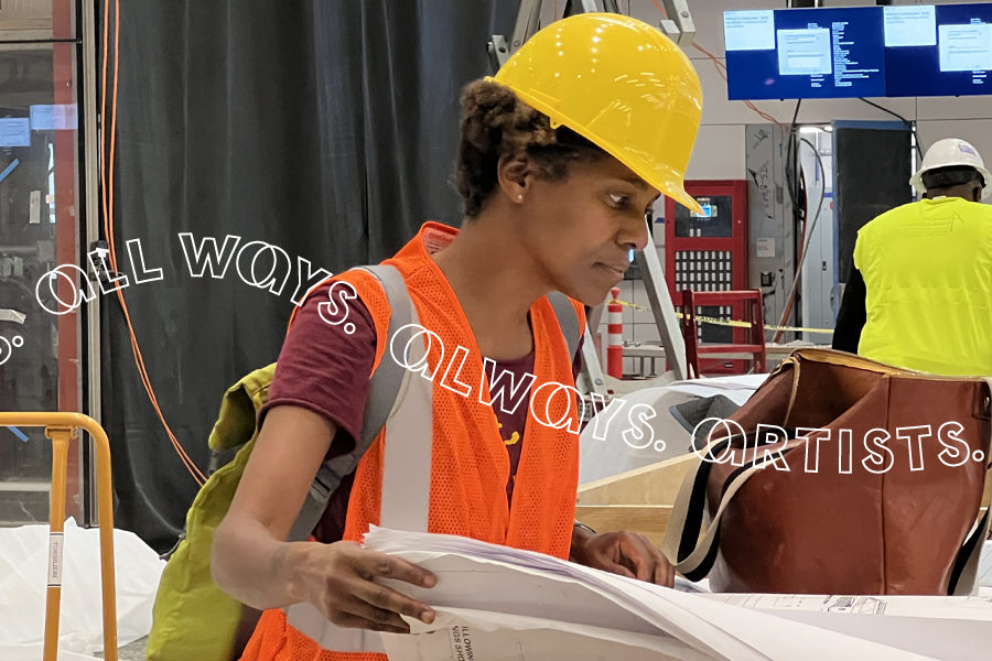 A Black woman in a hard hat and safety vest reviewing architectural plans for an installation.