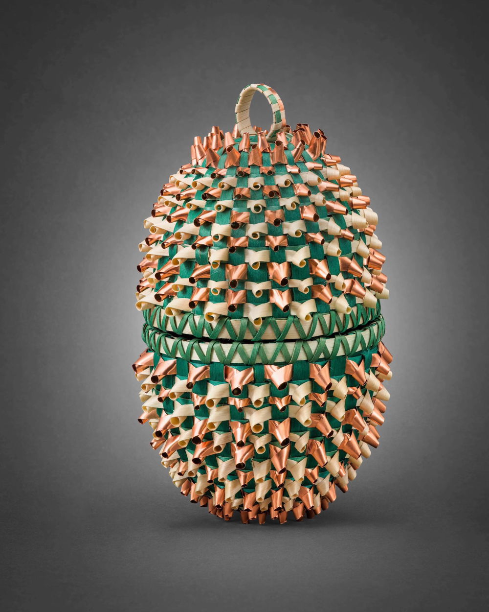 A woven, lidded sweetgrass basket in turquoise with golden accents. On either side of the basket is a green flash drive and a small glass specimen vial with a beetle inside.