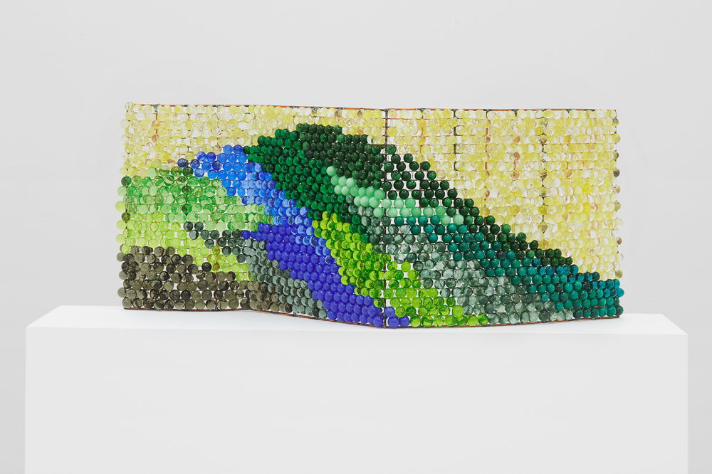 A free-standing screen covered in small circular beads. The rich blues, greens, and yellows of the stones create the image of a mountain peak.