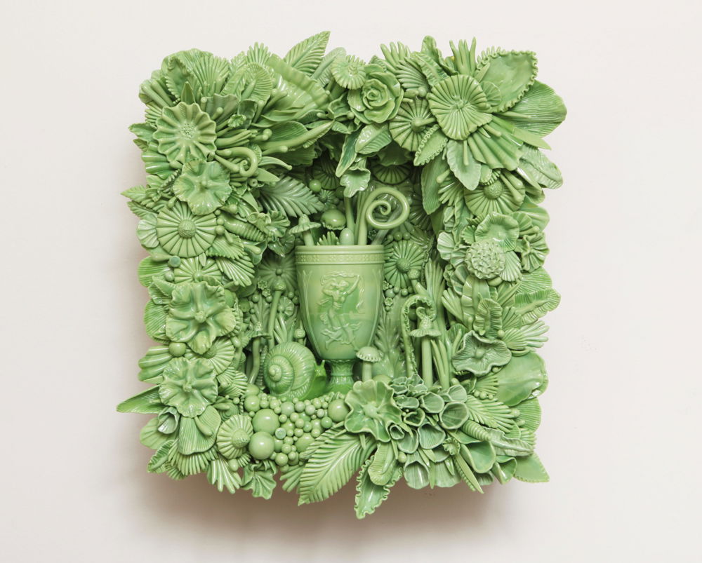 A rectangular glass wall sculpture of bright opaque green. In the center is a vase with the image of a goddess figurine floating with a scarf. There are flora, tendrils, feathers, mushrooms and assorted other organic matter coming out of the vase as well as around it. Next to the vase on the ground is a snail.