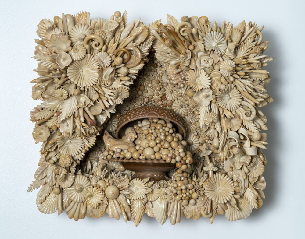 A rectangular wall sculpture entirely composed of and exploding with small, densely packed flowers, leaves, balls, and various botanicals sculpted from light brown opaque glass. Concave at its center, the sculpture cradles a shell holding a hen and overflowing with tiny balls.
