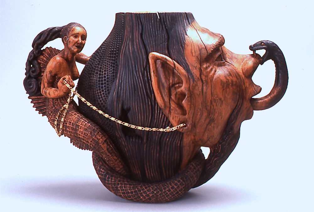 <em>Liar’s Vase</em> by Michelle Holzapfel, 1999. 3- axis turned Red Maple Burl Vase carved with Mermaid and Liar with Tongue biting Nose, found brass chain 'reins', 10 × 10 × 6 inches.