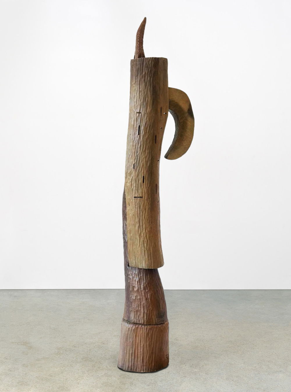 Photo of a tall wooden sculpture made of several pieces. At the top, a piece juts out like a horn, while another curves down like a banana.
