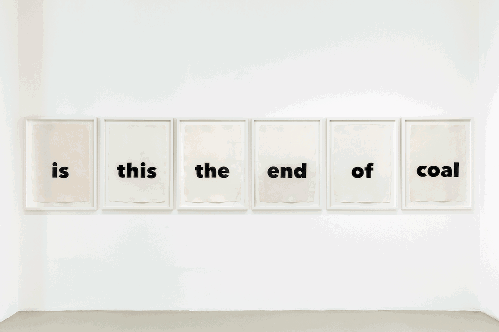 Six prints hung next to one another in white frames on a white wall. Each image has one word of black text on a white background that all together reads "is this the end of coal" from left to right.