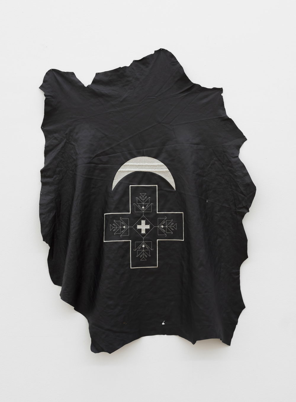 A piece of wrinkled black fabric on a white backdrop. Printed on the fabric is an upside-down crescent moon over a cross.