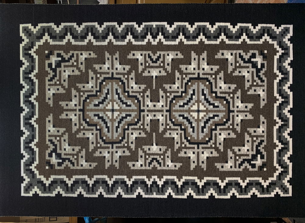 An intricate weaving composed in earthy browns and grays, organized around two central crosses surrounded by undulating patterns and geometric designs.