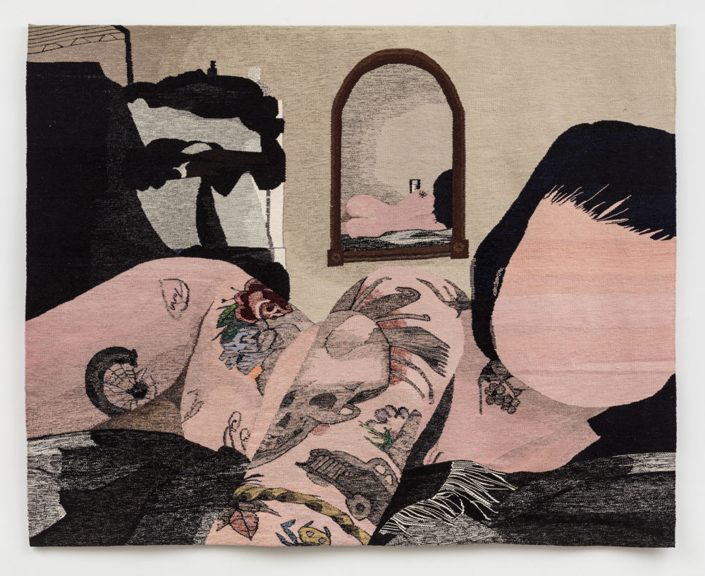 Hanging on a wall is a wool tapestry depicting a pale nude figure with tattoos in bed with a mirror behind them revealing their backside.