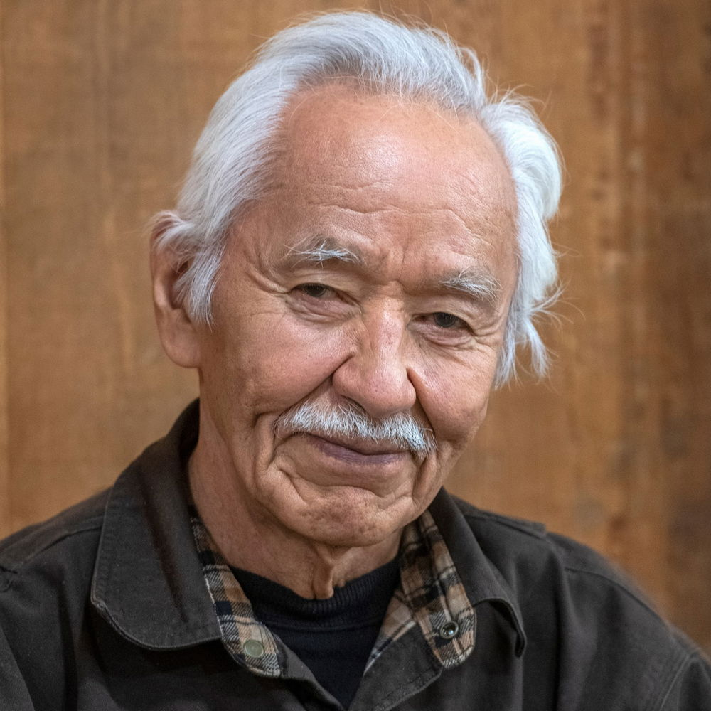 Nathan, a Tlingit man with tan skin and white hair, smiles warmly.