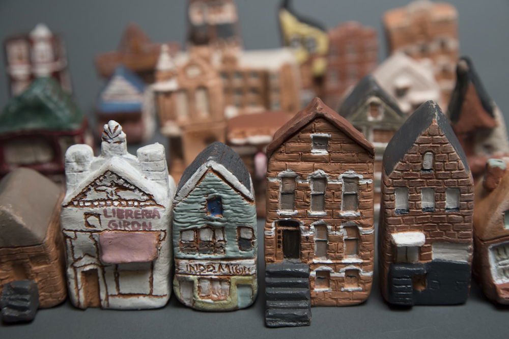 A row of miniature, hand-crafted ceramic row homes and stores. Other ceramic buildings are in the background, out of focus.