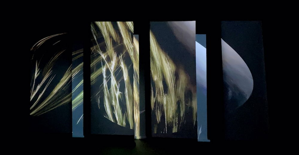 A photograph of a dark performance space, hung with fabrics covered with abstract images that look like streaks of light or electricity.