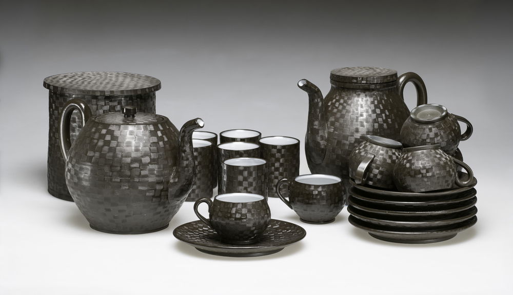 <em>BlackWare Group</em>, 2018. Black porcelainous clay, glaze with applied texture to capture reflection then salt fired, dimensions 9 x 28 x 14 inches. Service, storage, and display combines the subjects of kettle, box, two types of drinking cups, and sauce plate.