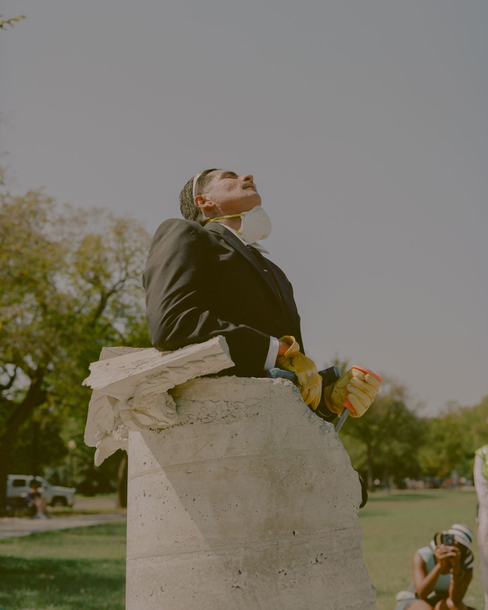 rafa is encased in a cement column from the waist down. He is wearing yellow work gloves and a protective facemask around his chin as he leans his face toward the sky.
