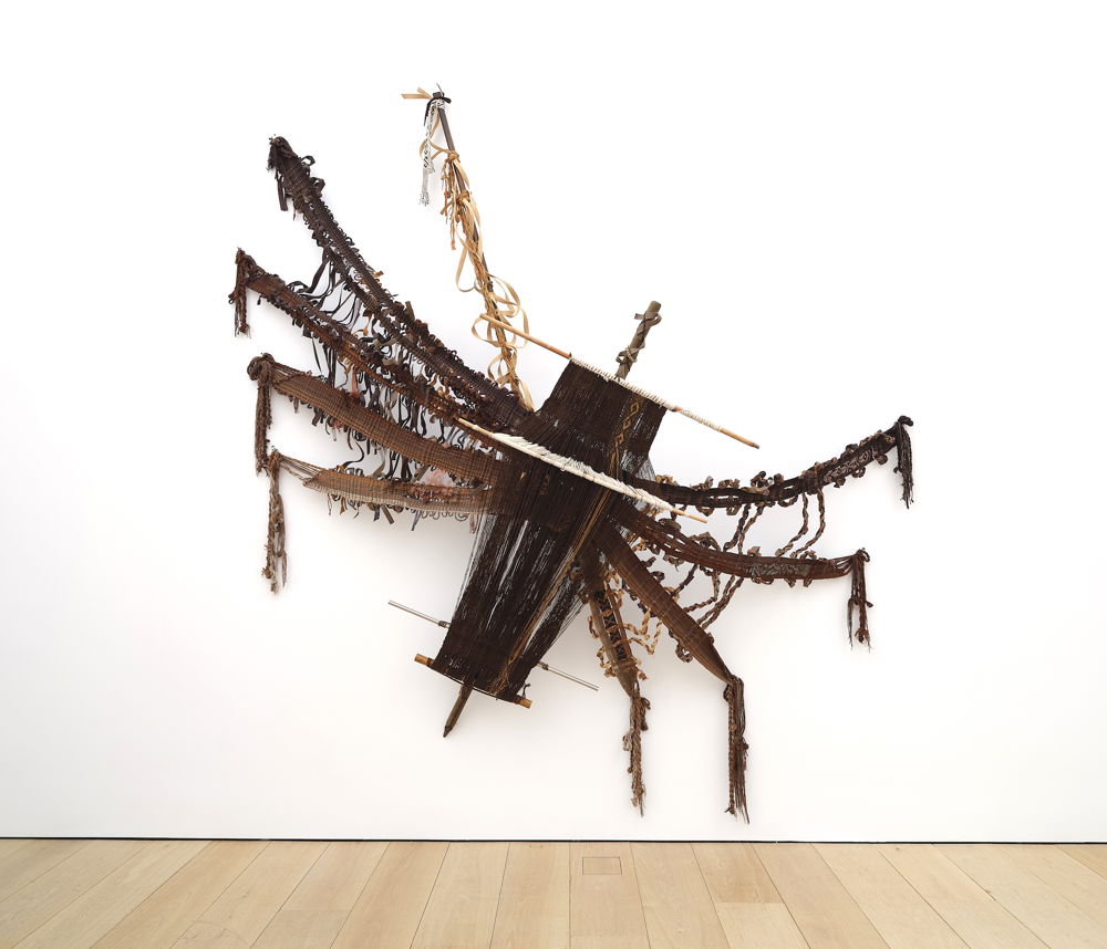 A multimedia textile where the artist has handwoven brown threads into the shape of a large spider. The artist has incorporated elements of the loom to add to the body and structure of the spider.