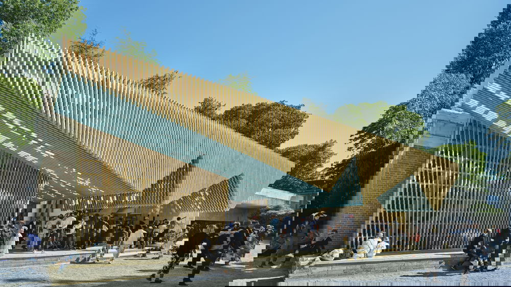 A timber and metal porch structure shelters a group of people from the sun.