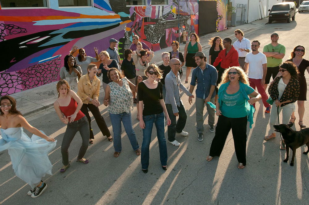 An overhead photo of Beth, smiling widely, candidly posing with a crowd of community members on a Miami concrete street.