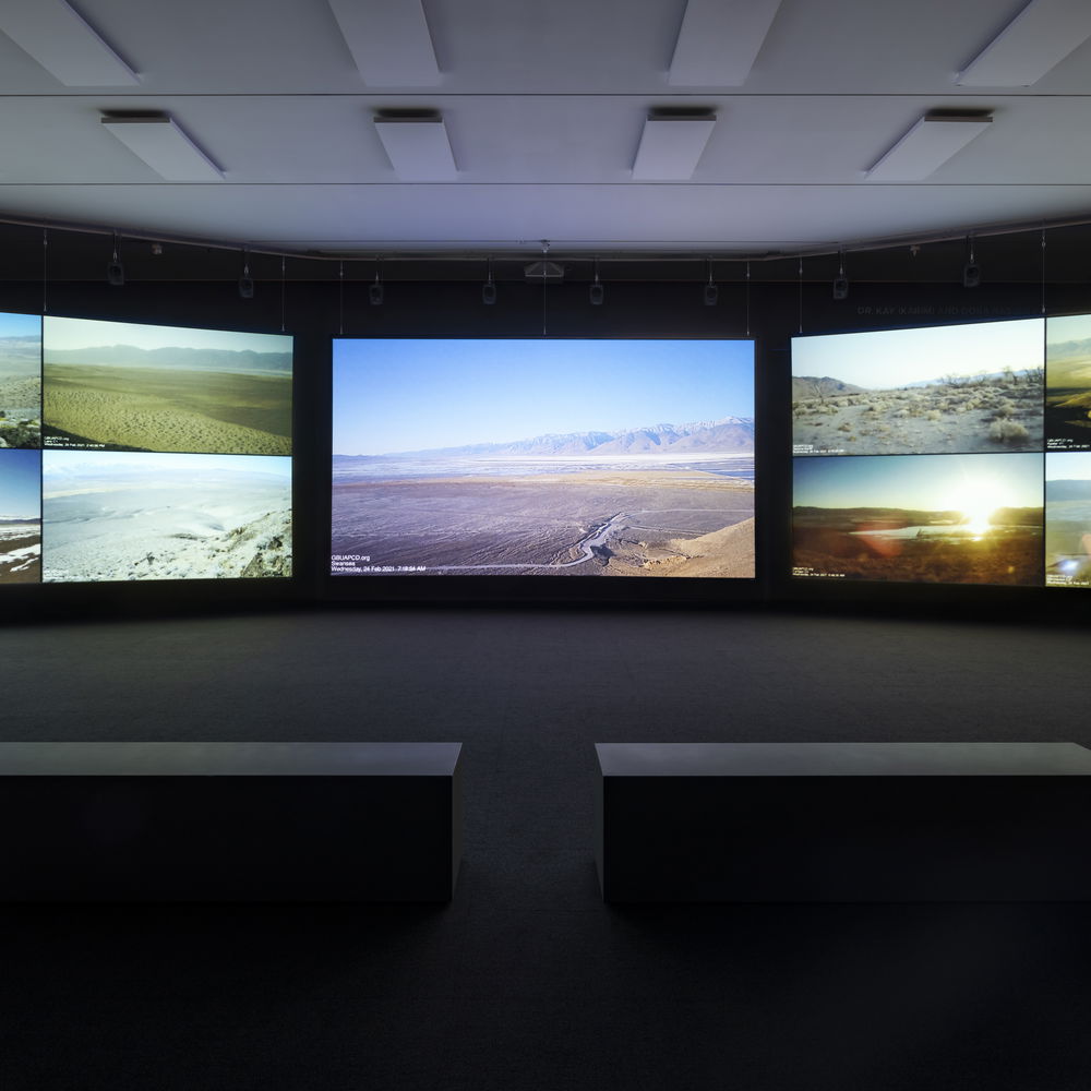 Nine images of landscapes, all featuring bodies of water, displayed on a surround-style projector. Two low-top rectangular benches are dimly lit in the center of what appears to be an exhibition-style projector room.