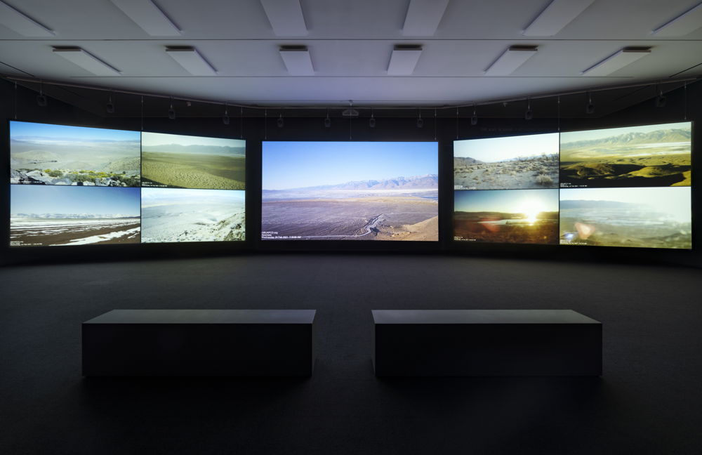 Nine images of landscapes, all featuring bodies of water, displayed on a surround-style projector. Two low-top rectangular benches are dimly lit in the center of what appears to be an exhibition-style projector room.