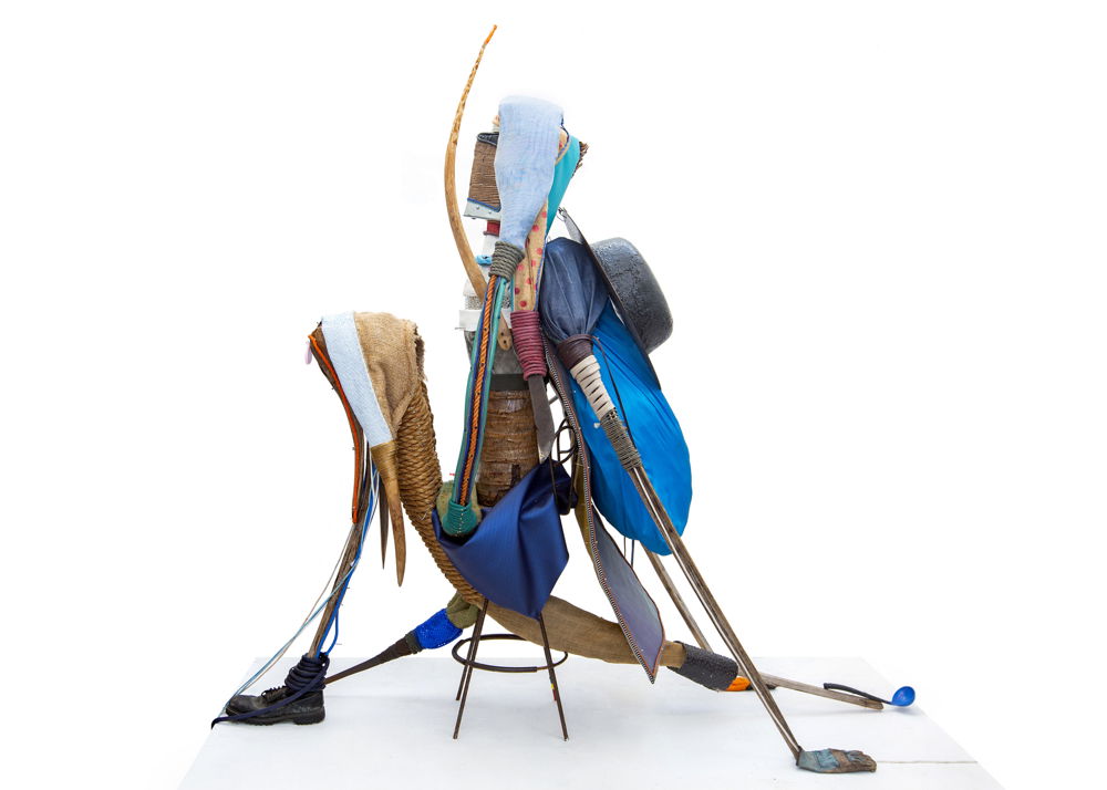 An assemblage of found objects in a triangular composition with a spindly stool at its base. Objects include a number of straight and curved rods, ropes, bags, and a black boot.