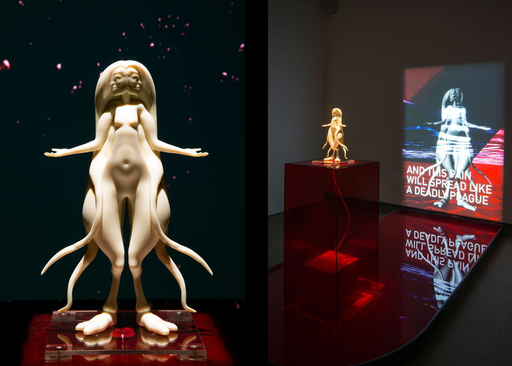 A white 3D mold of a feminine humanoid with their head split into two faces, billowing hair, broad curved hips, large hooves, and fluid tentacles. The mold sits on a red, translucent display in front of a projection.