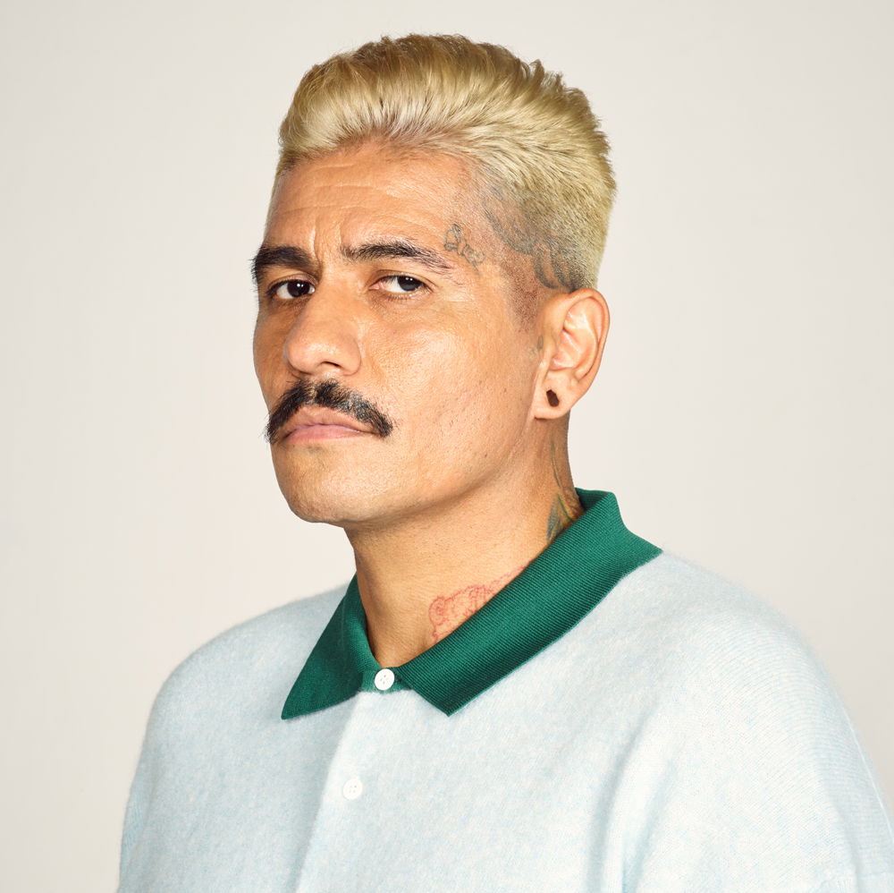rafa, a man with blonde hair, brown skin, and a black mustache, looks sidelong at the camera. He wears a sea foam green shirt with a dark green collar.