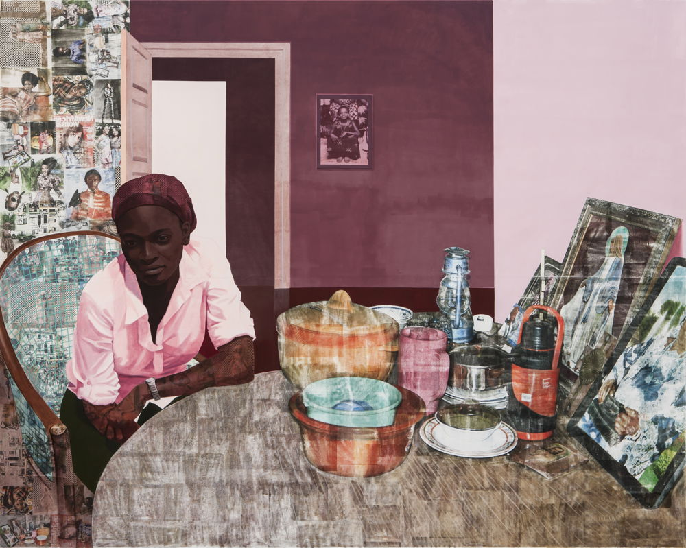 A Black woman sits at a kitchen table where pots, plates, and framed photos are displayed. The woman leans on the table in a head scarf and shirt and looks pensively. Photos of Black figures decorate the background room.