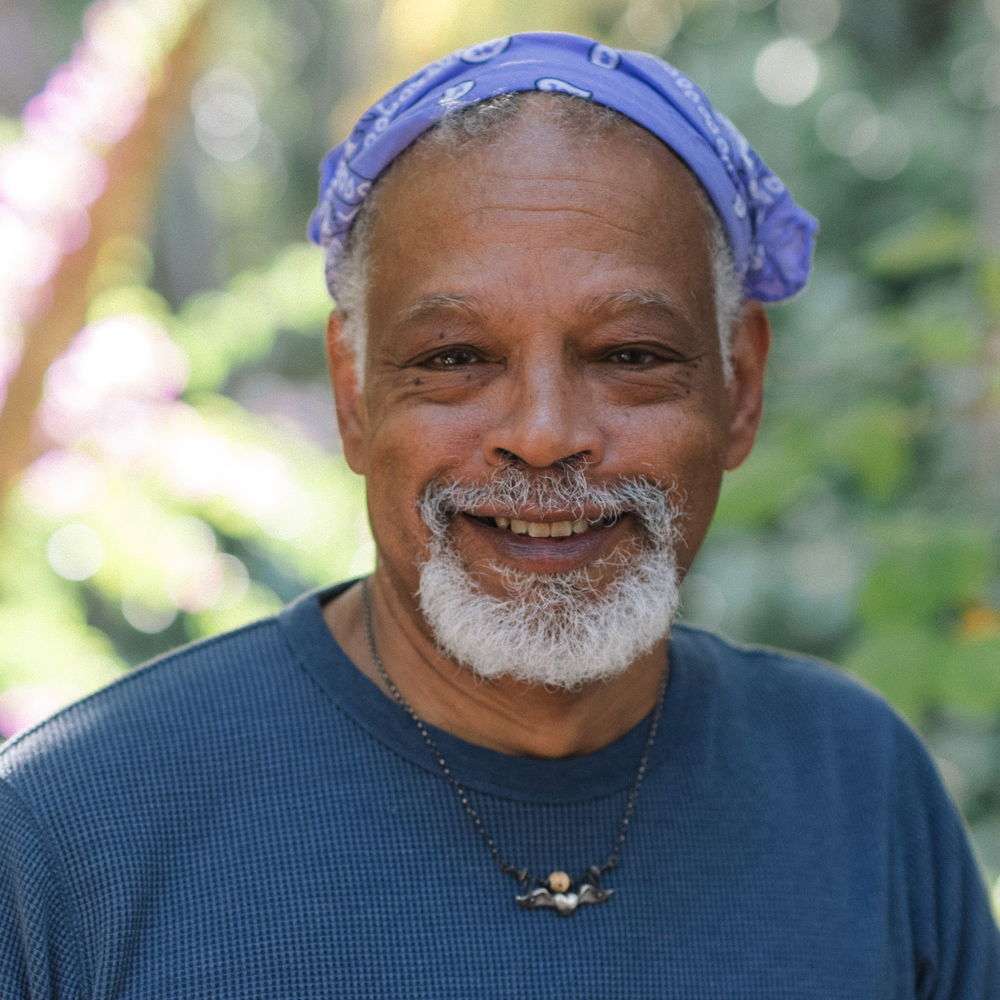 Ishmael, a man with a gray goatee and wearing a lavender bandana on his head, smiles warmly.