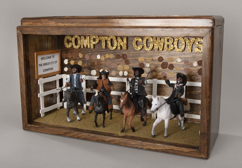 A diorama with four stylized miniature sculptures of Black cowboys riding four horses. While the cowboys look hand-crafted, the horses appear to be store-bought and machine-made. Behind the figurines is a white fence and multicolored dots representing faces in a crowd. Hovering at the top of the display are glittering gold letters that read, "Compton Cowboys."