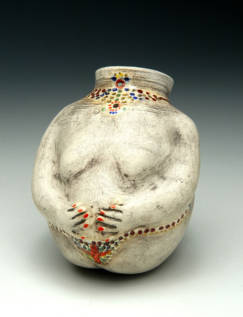 A ceramic vessel shaped like the body of a person whose arms meet in the center and are painted with red fingernails. Dots of color surround the neck and the bottom of the vessel like a jeweled necklace and belt.